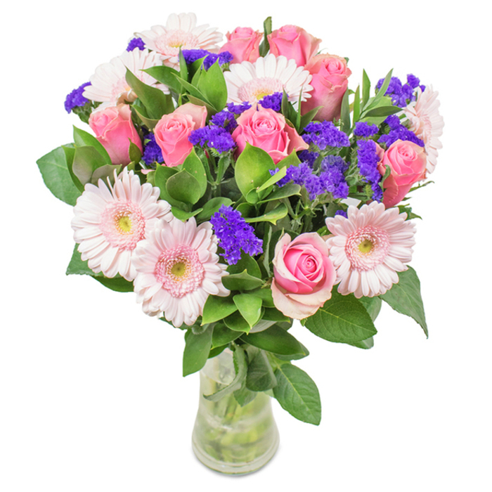 This elegant arrangement, presented in a sleek, clear glass vase, captures the essence of Muswell Hill's vibrant floral artistry. At its heart, seven to nine pink roses unfurl in classic spirals, their petals ranging from tightly budded to just-blossoming-shades that glow gently in the natural light often found spilling through homes along Cranley Gardens. These elegant roses are paired with five to seven pale pink Gerbera daisies, their round blooms and finely radiating petals surrounding subtle white centres. Deep purple statice is thoughtfully interspersed, injecting a playful texture and a dramatic, modern flair that's reminiscent of the colourful weekend markets at Muswell Hill's heart. The lush greenery frames the bouquet, offering a rich base, each leaf cool and glistening as if fresh from the gardens behind Firs Avenue. The transparency of the vase, with visible stems and shimmering water, underlines the bouquet's freshness and careful hand-tying-a harmonious design suitable for birthdays, anniversaries, Mother's Day, or as a uplifting decorative accent for local homes and studios, radiating joy and affection shaped by Muswell Hill expertise.